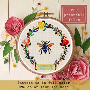 Può includere: Schema di punto croce con un'ape con una ghirlanda di fiori intorno. Il motivo include il testo "beautiful beeyotch".