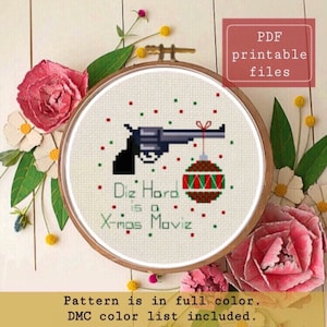 Può includere: Schema di punto croce con una pistola con un ornamento natalizio appeso alla canna. Il testo dice "Die Hard is a Xmas Moviz".