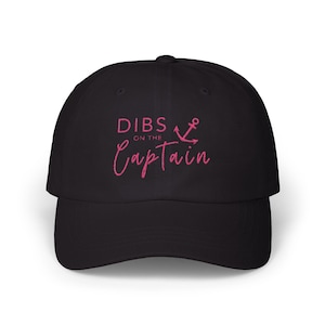 May include: Black baseball cap with pink embroidery that reads "DIBS ON THE CAPTAIN" with an anchor symbol.