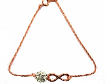 May include: A rose gold infinity bracelet with a small crystal ball charm. The bracelet is made of a delicate chain.