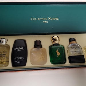 Op de afbeelding: Een geschenkset met miniatuurparfums in een groene doos met het opschrift "Collection Homme Paris". De set bevat zes verschillende parfumflesjes in diverse vormen en kleuren, waaronder een groene fles met een gouden dop en een zwarte fles.