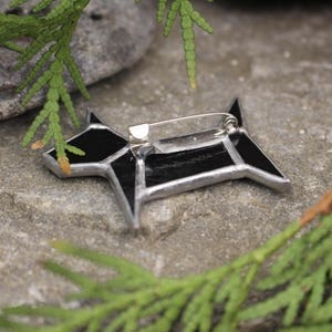 Pode incluir: Broche de vidro preto em forma de c&atilde;o com um alfinete de prata sobre um fundo de pedra cinza.
