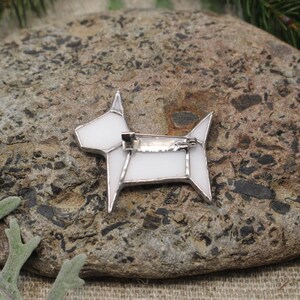 Op de afbeelding: Witte glazen honden broche met een zilveren pin. De broche heeft de vorm van een hond met een eenvoudig geometrisch ontwerp.