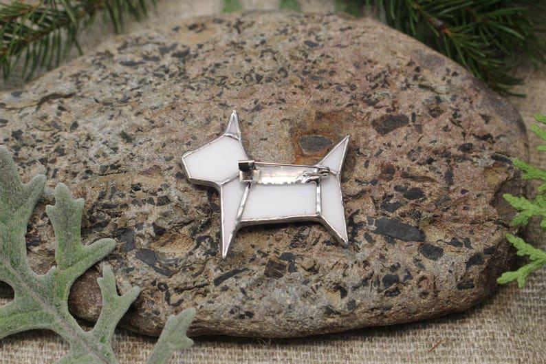 Op de afbeelding: Witte glazen honden broche met een zilveren pin. De broche heeft de vorm van een hond met een eenvoudig geometrisch ontwerp.