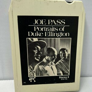 May include: A white cassette tape with a black label. The label features a black and white photo of three men. The text on the label reads "Joe Pass Portraits of Duke Ellington" and "Stereo 8 S10-716".