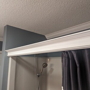 May include: A bathroom interior featuring a white shower stall with a dark gray shower curtain. The showerhead is visible. White crown molding adorns the ceiling and the top of the shower stall. The walls are painted in shades of gray and blue.