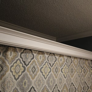 May include: White crown molding above a patterned curtain. The curtain features a repeating design in gray, yellow, and white. The ceiling is a textured brown color, and the wall is a dark gray.