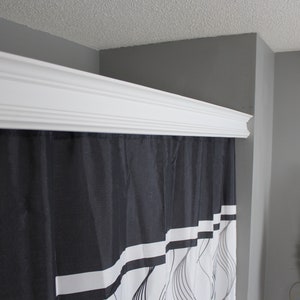 May include: A white decorative crown molding is installed above a black and white shower curtain. The shower curtain has a geometric design with white stripes and curved lines. The walls are painted gray.
