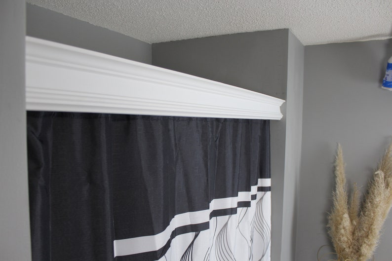 May include: A white decorative crown molding is installed above a black and white shower curtain. The shower curtain has a geometric design with white stripes and curved lines. The walls are painted gray.