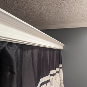 May include: A white crown molding adorns the top of a shower curtain. The shower curtain is black with white vertical stripes and a flowing, abstract design. The ceiling is textured and painted a light beige.
