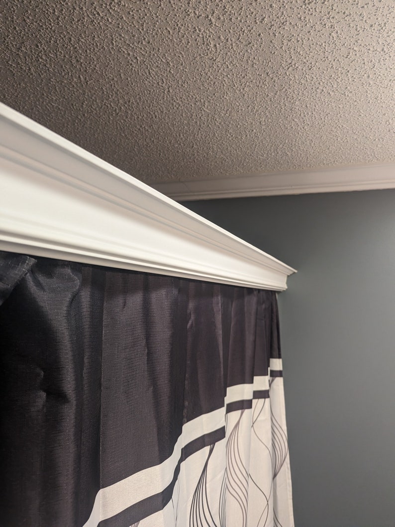 May include: A white crown molding adorns the top of a shower curtain. The shower curtain is black with white vertical stripes and a flowing, abstract design. The ceiling is textured and painted a light beige.