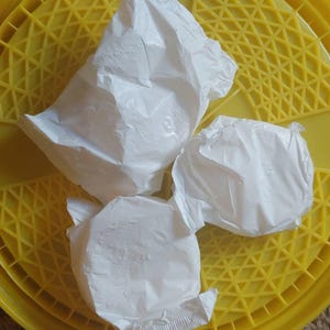 May include: Three white, crinkled, paper-like pouches are sitting on a yellow, honeycomb-patterned surface.