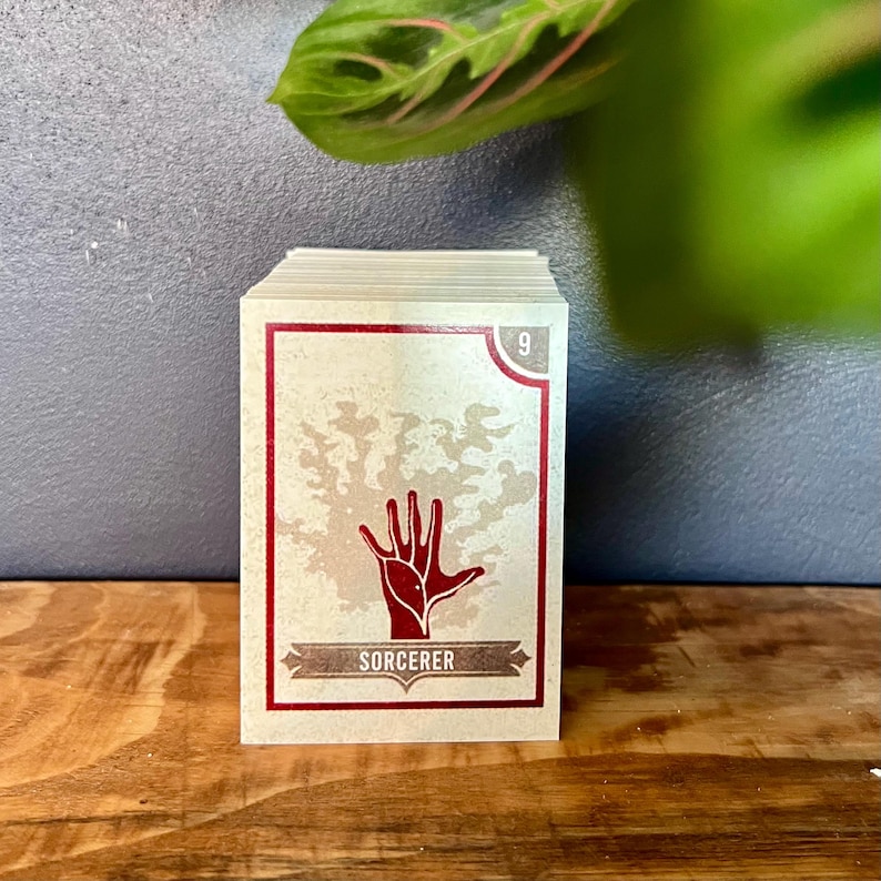 May include: A deck of cards with a red hand and the word "SORCERER" on a beige card with a red border. The card is numbered "9".