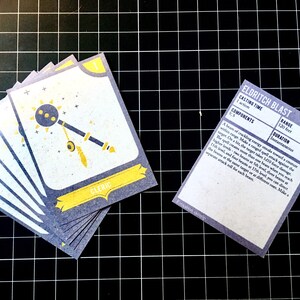 May include: A set of six blue and yellow playing cards with a cleric symbol and the text "CLERIC". A separate card with the text "ELDRITCH BLAST" and details about the spell's casting time, components, range, and duration.
