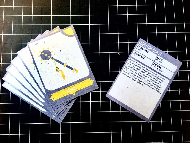 May include: A set of six blue and yellow playing cards with a cleric symbol and the text "CLERIC". A separate card with the text "ELDRITCH BLAST" and details about the spell's casting time, components, range, and duration.