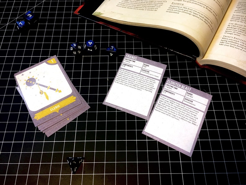 May include: A close-up of a tabletop game with cards featuring the text "Friends", "Eldritch Blast", and "Cleric". The cards are on a black grid surface with blue dice scattered around.
