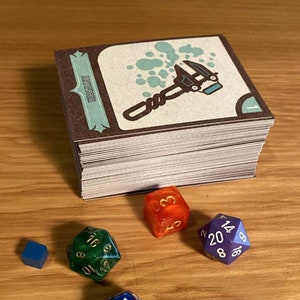 May include: A stack of brown and white cards with a blue and white illustration of a wrench on the top card. The text "AUTO REPAIR" is visible on the card. There are four dice on a wooden surface: one blue, one green, one orange, and one purple.