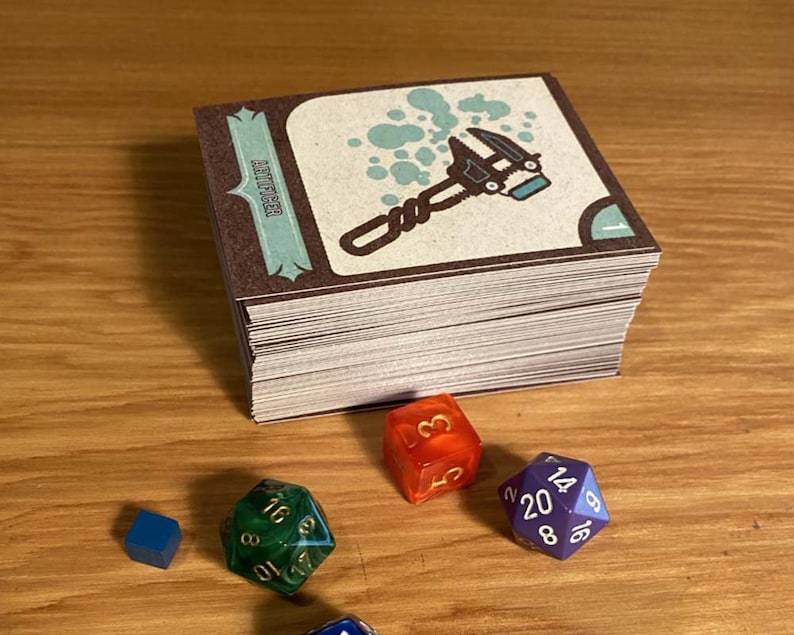 May include: A stack of brown and white cards with a blue and white illustration of a wrench on the top card. The text "AUTO REPAIR" is visible on the card. There are four dice on a wooden surface: one blue, one green, one orange, and one purple.
