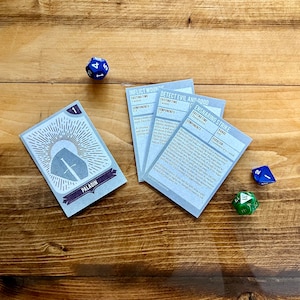 May include: Four blue and white cards with text about the Dungeons and Dragons game. The cards are on a wooden table with two dice, one blue and one green.