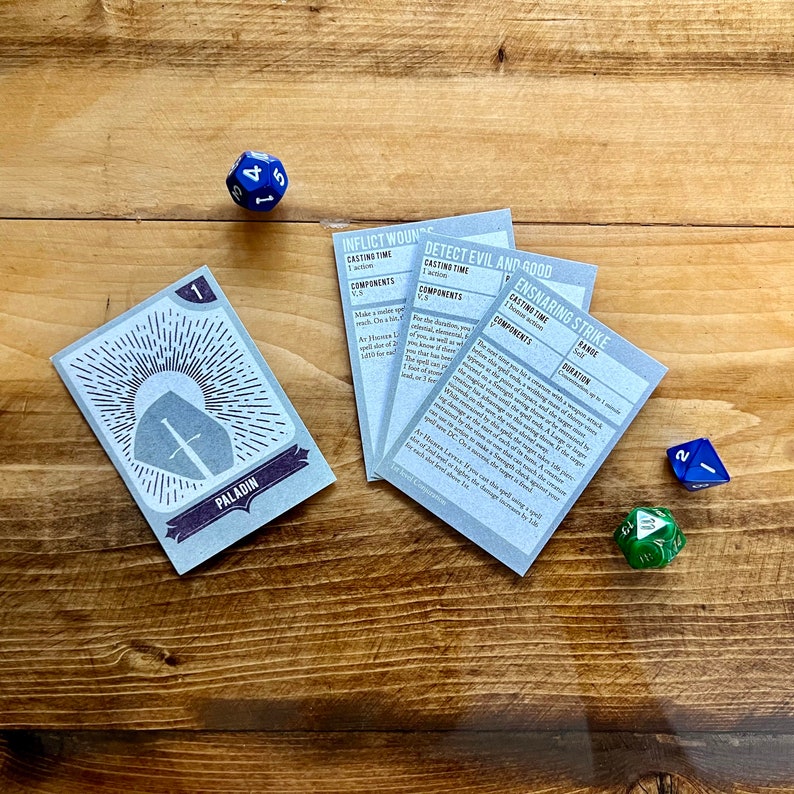May include: Four blue and white cards with text about the Dungeons and Dragons game. The cards are on a wooden table with two dice, one blue and one green.