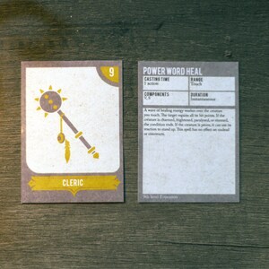 May include: A card game for Dungeons and Dragons featuring a cleric character with a mace and a spell card for Power Word Heal. The card is a light brown colour with black text and a yellow border.