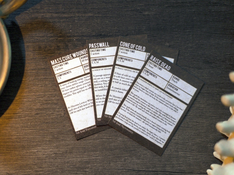 May include: Five black cards with white text describing different spells. The spells are "Mass Cure Wounds", "Passwall", "Cone of Cold", "Raise Dead", and "Cure Wounds".