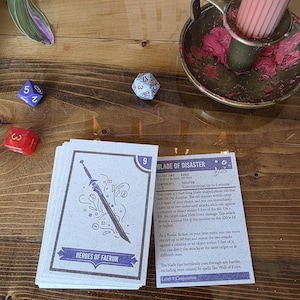 May include: A stack of fantasy game cards with a sword illustration and the text "HEROES OF FAERUN". A red, blue, and white die are scattered on a wooden surface, along with a candle holder and a lit candle.