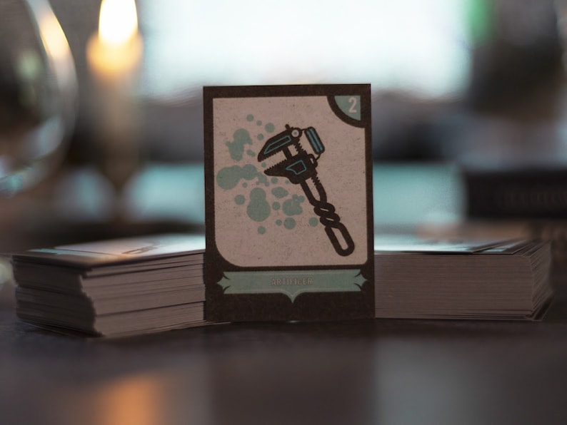 May include: A card game card with a brown background and a light brown border. The card has a number "2" in the top right corner. The card has a blue and black illustration of a wrench. The card has the word "ADJUSTER" in the bottom center.