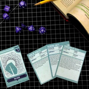 May include: A set of five blue and white dice and four cards with text that reads "Paladin", "Aura of Vitality", "Blinding Smite", and "Guardian of Faith".