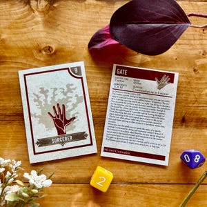May include: Two cards from a Dungeons and Dragons game. The card on the left is a Sorcerer card with a hand reaching out from a tree. The card on the right is a Gate card with a description of the spell. The card is brown with red text.