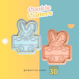 May include: Two cookie cutters in the shape of a bunny rabbit peeking over a sign. The cutters are made of blue and pink plastic. The text "Cookie Cutters" is in the top left corner of the image. The text "@SWEET3D.SHOP" is in the bottom left corner of the image. The text "SWEET 3D" is in the bottom right corner of the image.