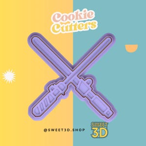 May include: Purple plastic cookie cutters shaped like two crossed lightsabers. The text "Cookie Cutters" is above the cutters and the text "@SWEET3D.SHOP SWEET 3D" is below the cutters.