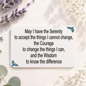 May include: A rectangular white card featuring the black printed text: May I have the Serenity to accept the things I cannot change, the Courage to change the things I can, and the Wisdom to know the difference. Small blue floral accents appear.