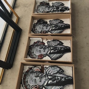 May include: Four framed black and white illustrations of Albert Einstein wearing headphones. The illustrations are in cardboard boxes with white foam padding.
