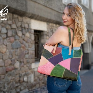 May include: A rectangular tote bag constructed from multi-coloured leather patches in shades of pink, purple, teal, green, and tan. The bag features visible decorative stitching along the seams and two leather shoulder straps in tan and green.
