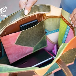 May include: A multi-coloured leather tote bag featuring a patchwork design in shades of olive green, pink, brown, and light blue. The interior includes a central pocket, a zippered compartment, and visible stitching along the edges.