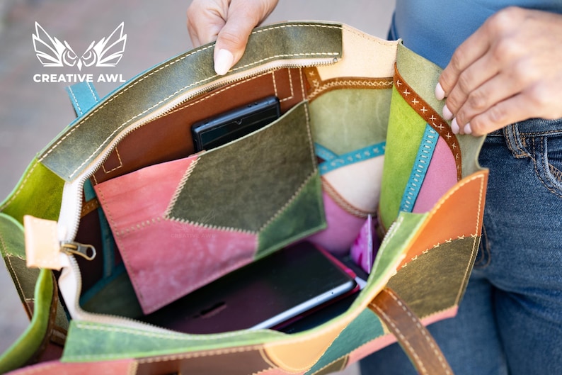 May include: A multi-coloured leather tote bag featuring a patchwork design in shades of olive green, pink, brown, and light blue. The interior includes a central pocket, a zippered compartment, and visible stitching along the edges.