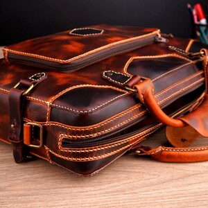 May include: A brown leather briefcase with a top handle and a zippered closure. The briefcase has a distressed look and is made of high-quality leather.