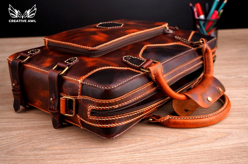 May include: A brown leather briefcase with a top handle and a zippered closure. The briefcase has a distressed look and is made of high-quality leather.
