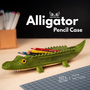 May include: A green alligator-shaped pencil case with a yellow eye and a row of teeth. The pencil case holds several colored pencils. The words "Alligator Pencil Case" are displayed in white text.