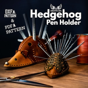 May include: A leather hedgehog pen holder with a brown body and green accents. The holder is filled with sewing needles and a small awl. The image also includes spools of thread in various colors and a pair of scissors.