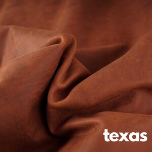 May include: Close-up of a brown leather fabric with a textured surface. The fabric is folded and draped, creating a soft, natural look. The word "texas" is printed in white letters at the bottom of the image.