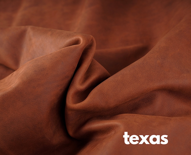May include: Close-up of a brown leather fabric with a textured surface. The fabric is folded and draped, creating a soft, natural look. The word "texas" is printed in white letters at the bottom of the image.