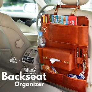 Può includere: Un organizer in pelle color cuoio per il sedile posteriore dell'auto con molteplici scomparti, tra cui un porta scatola di fazzoletti, passanti per penne, una tasca per bottiglia d'acqua e fessure superiori per riviste e matite.