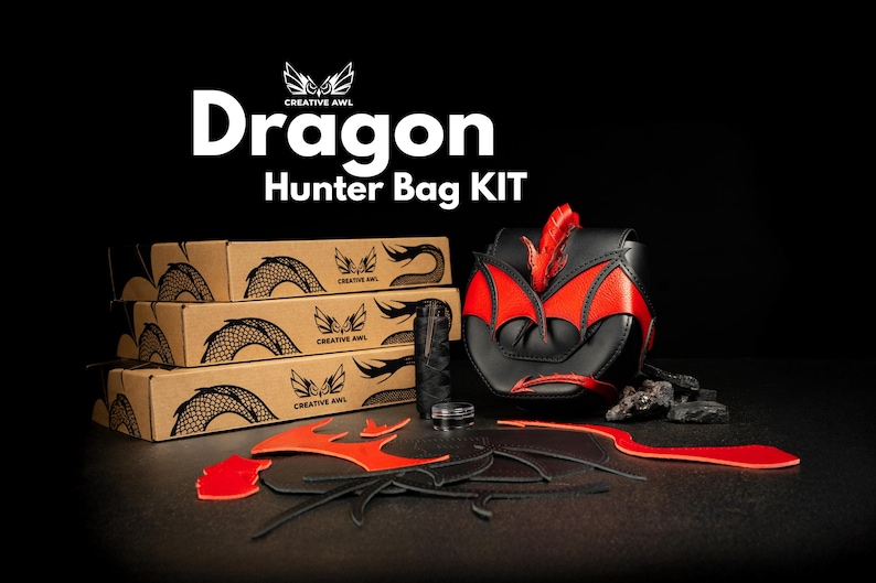 Op de afbeelding: Een Dragon Hunter Bag KIT met drie gestapelde kartonnen dozen met draak-schubillustraties, een gemonteerde zwart-rode lederen tas en diverse losse rode en zwarte lederen onderdelen, zwart garen en een klein bakje.