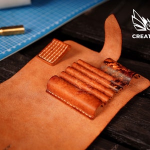 May include: A brown leather case with multiple slots for holding tools. The case is open and the slots are visible. The case is made of leather and has a stitched edge.