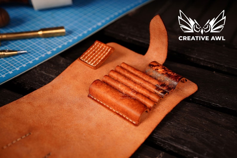 May include: A brown leather case with multiple slots for holding tools. The case is open and the slots are visible. The case is made of leather and has a stitched edge.