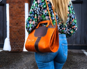 May include: A brown and orange leather tote bag with a shoulder strap. The bag has a top handle and a logo that says "Creative AWL".