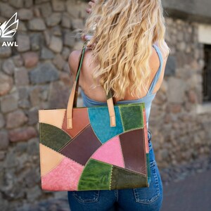 May include: A rectangular tote bag constructed from multi-coloured leather patches in shades of pink, green, brown, and blue. The bag features two light tan leather shoulder straps and visible stitching along the edges of each leather panel.