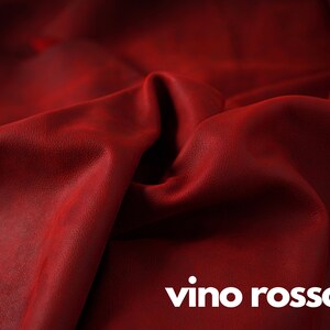 May include: Close-up of a deep red leather fabric with a textured surface. The fabric is folded and draped, creating soft folds and curves. The text "vino rosso" is printed in white at the bottom of the image.